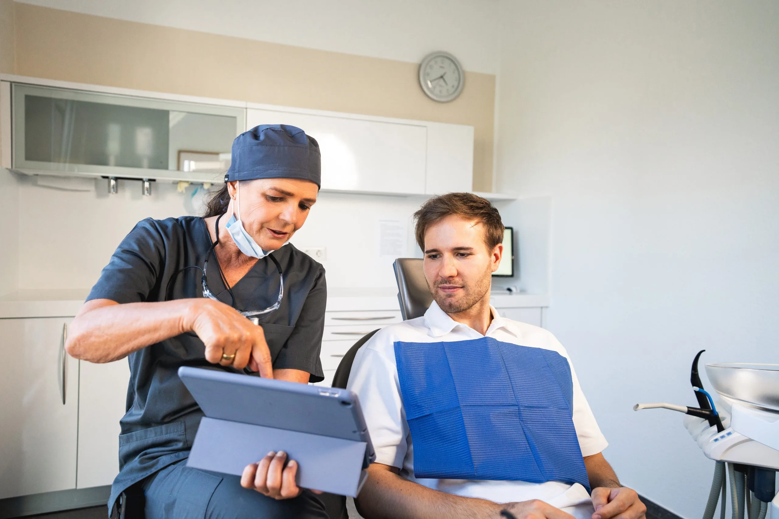 Zahnarzt zeigt Patient auf einem Tablet die Behandlung